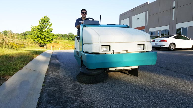 technician using a Tennant rider floor sweeper in a parking lot