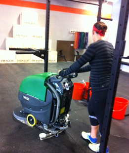 person disinfecting and cleaning a rubber gym mat with the a Bulldog floor scrubber