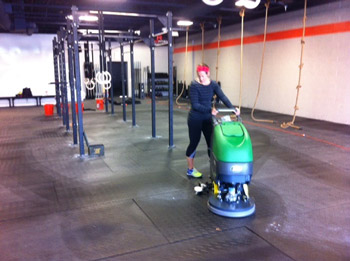 person cleaning and disinfecting gym mats with an industrial floor scrubber