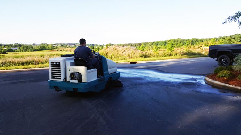 worker cleaning a driveway and parking lot with a Tennant industrial floor sweeper