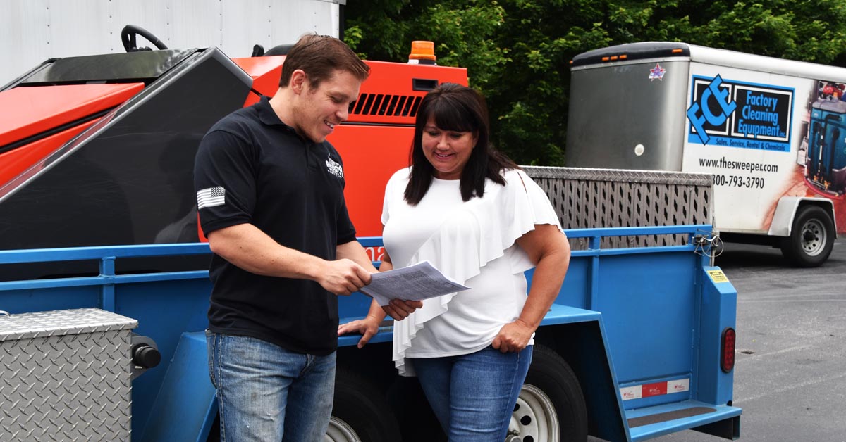 client reviewing paperwork with FCE employee next to a floor scrubber available for rent