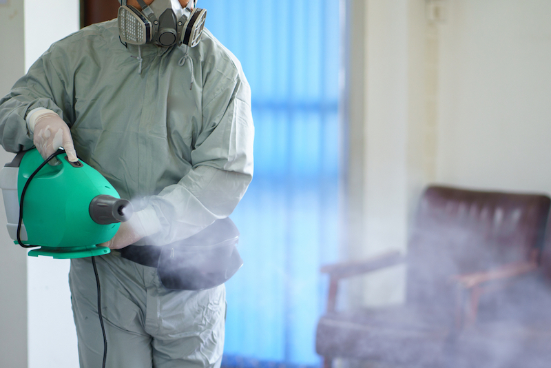 worker in hazmat suit using electrostatic disinfectant spayer in office