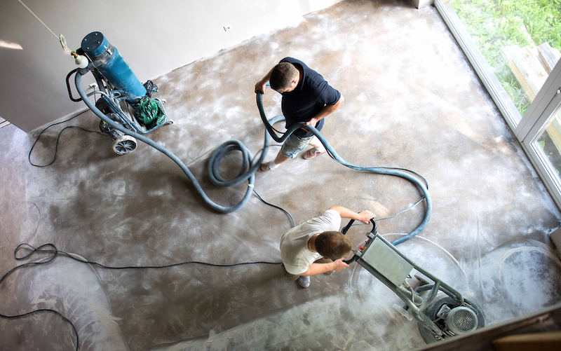 workers using concrete grinder and dust collector to prep floor for epoxy coating
