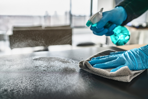 hands wearing gloves spraying disinfectant and wiping table