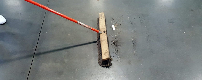 large broom being used to sweep debris on concrete warehouse floor