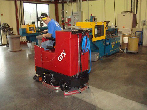 floor scrubber operator driving ride-on floor scrubber in a machine shop