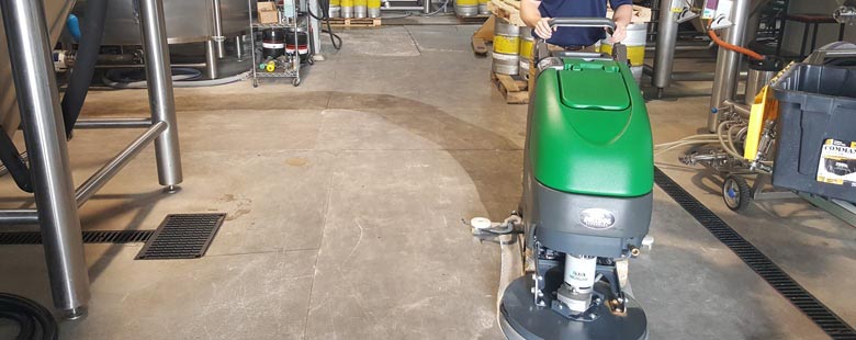 worker pushing Bulldog walk behind floor scrubber across concrete brewery floor