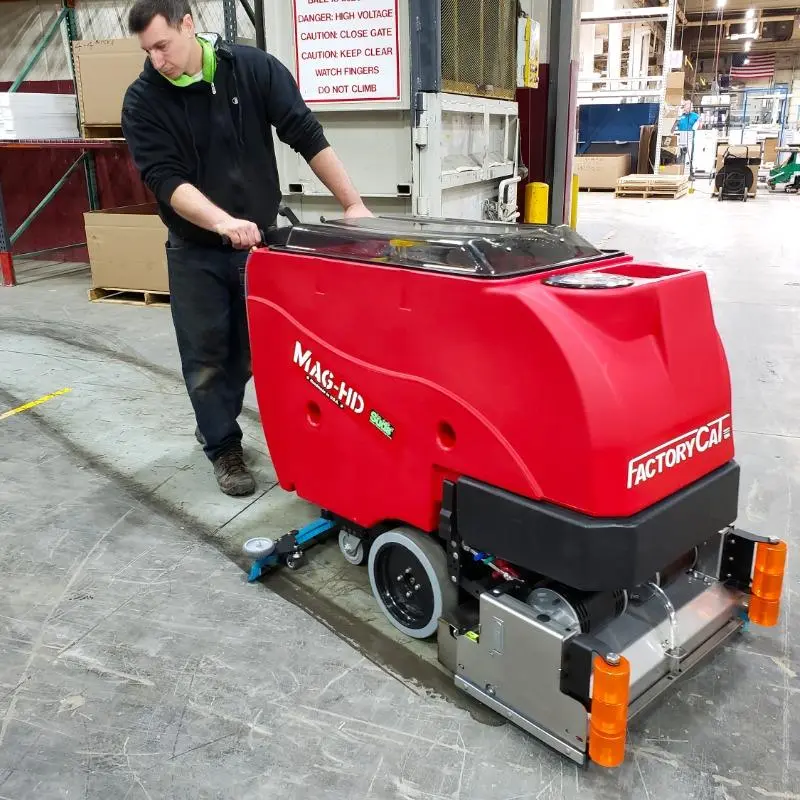 technician pushing red factory cat walk behind floor scrubber across concrete floor