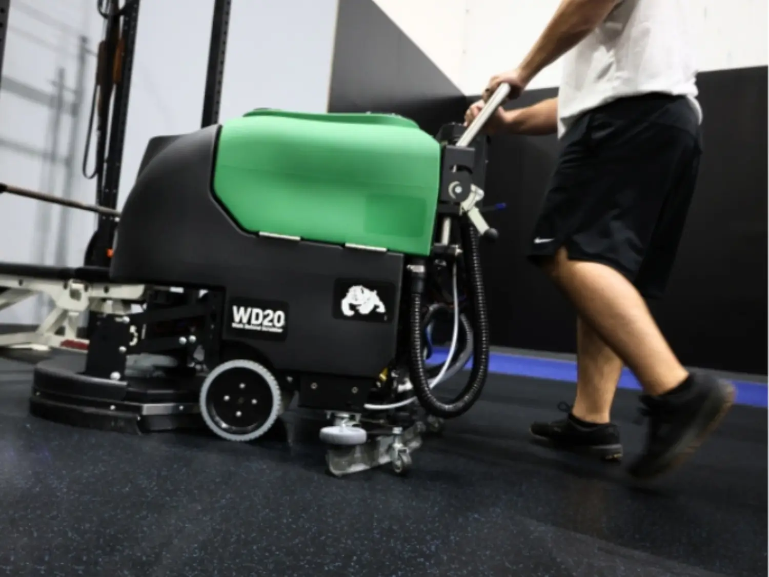 gym owner wearing white tshirt and black shorts pushing bulldog gym mat scrubber machine